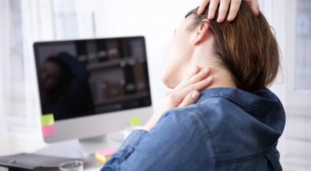 Worker sitting at desk stretching neck suggesting it may be tight or uncomfortable.