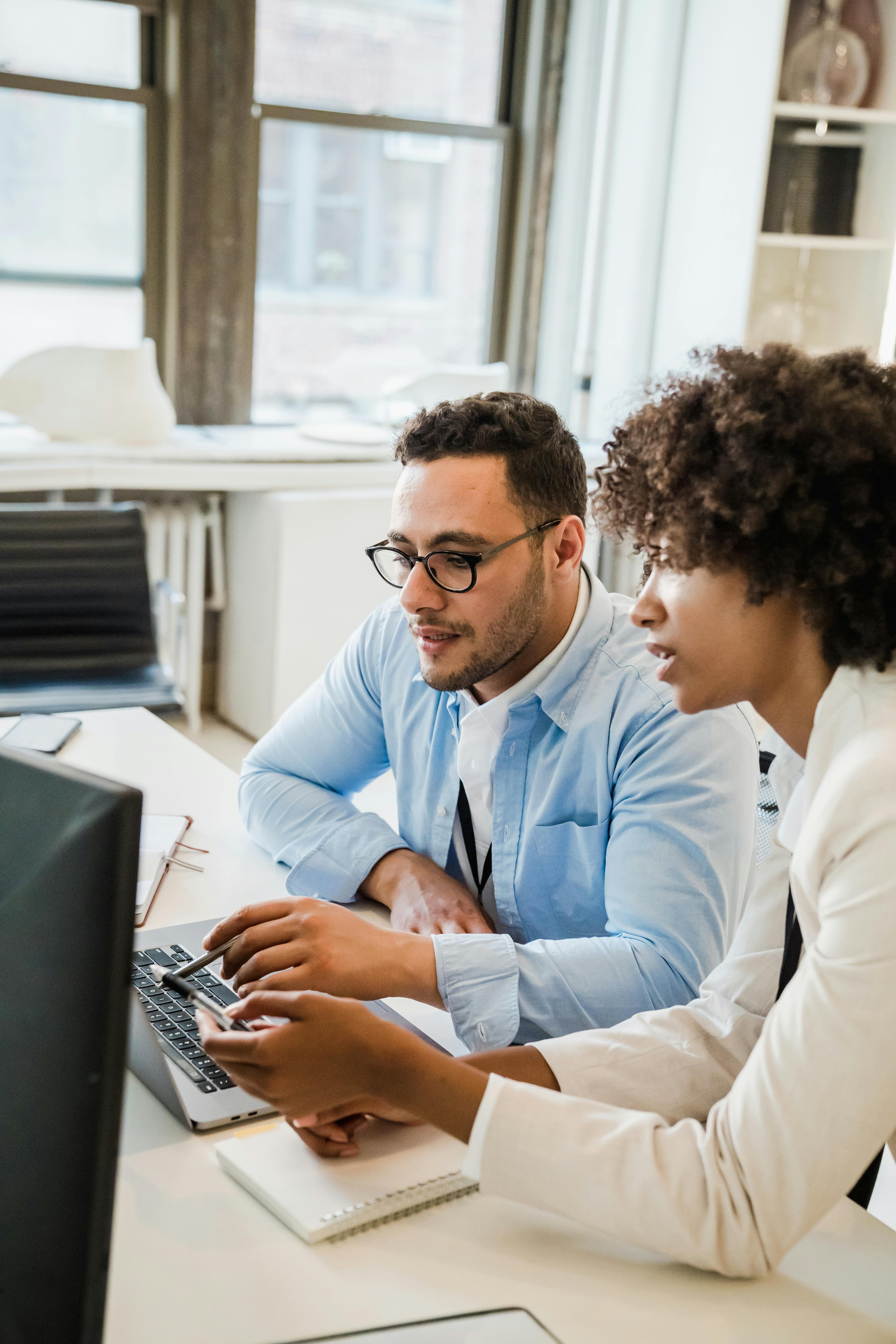 two people sitting beside each other at a computer workstation appearing to be working together.