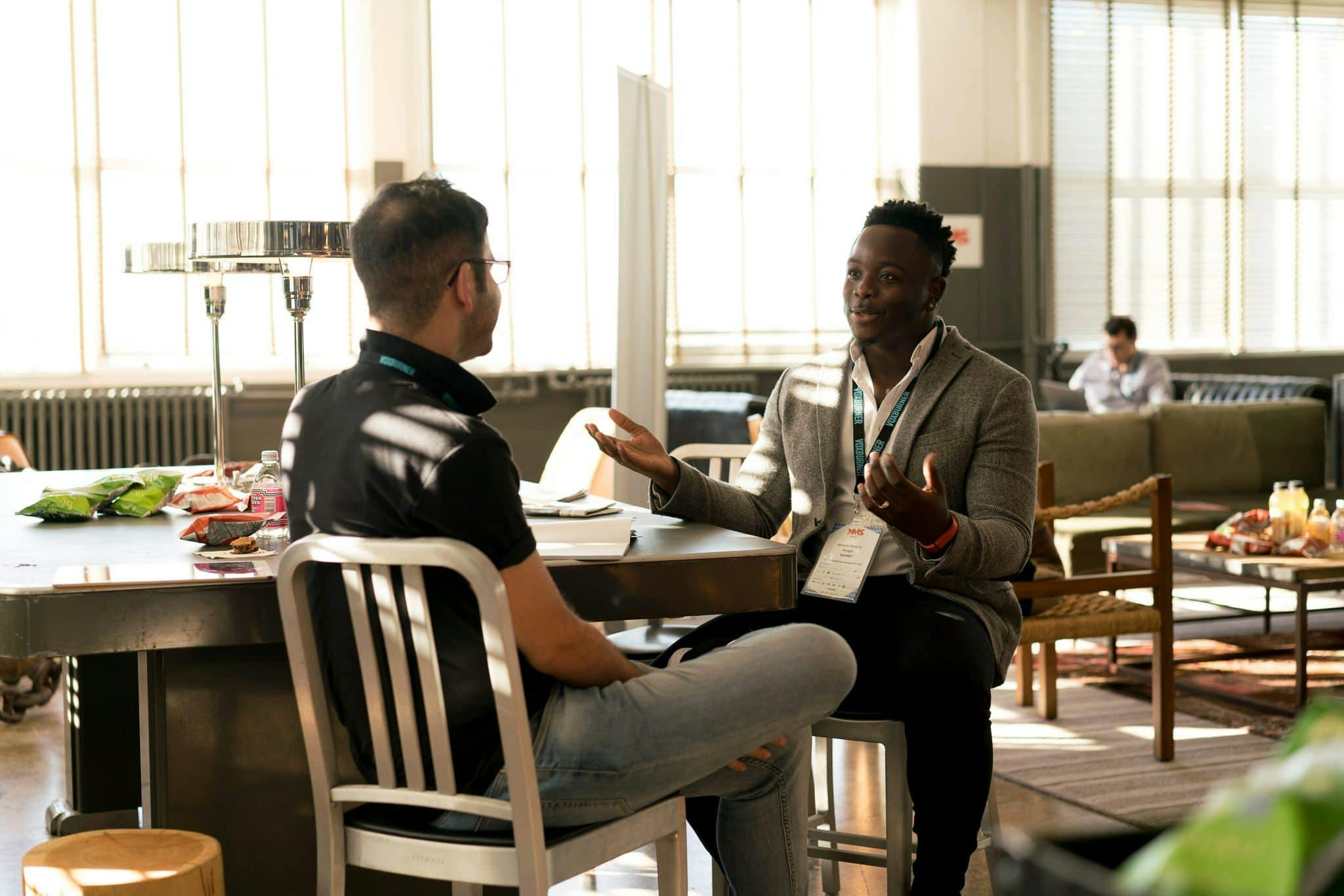 two people sitting and talking to each other. one with arms open and talking, the other listening with face away from camera.